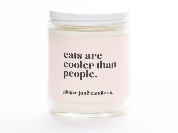a white jar candle with a light pink label that reads "Cats are Cooler Than People"