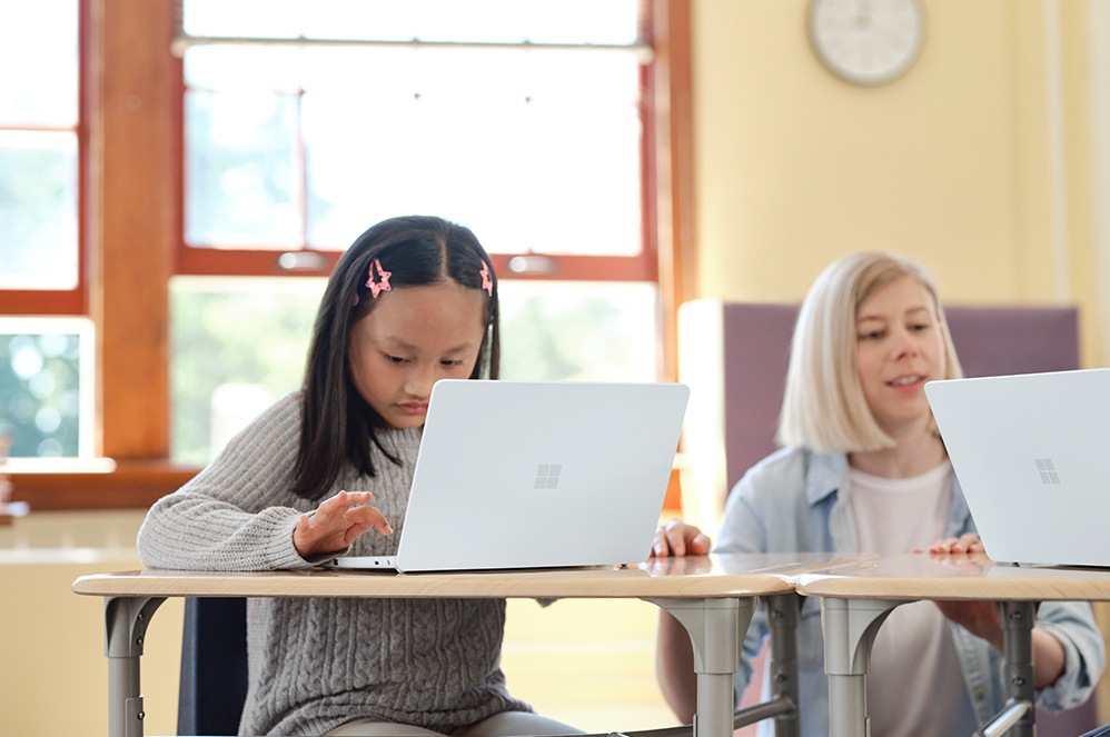 A child uses Surface Laptop SE on the carpet in a classroom.