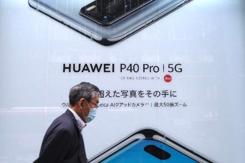 This picture taken on June 27, 2020 shows a man in Tokyo passing an advertisement for Huawei's 5G-capable smartphone; Apple is e